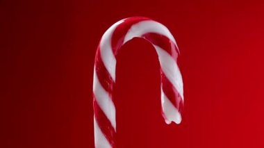 Alternatif kırmızı ve beyaz çizgili klasik bir şeker kamışının büyüleyici yakın plan videosu, parlak kırmızı bir arka fona karşı tatlı beyaz bir jöleyle kaplanıyor.