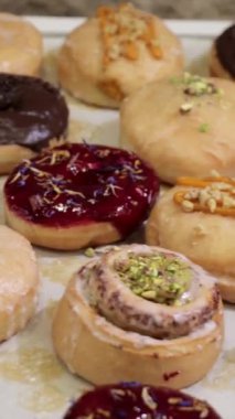 Fıstık, nane şekeri, çikolata jölesi gibi canlı malzemelerle süslenmiş vejetaryen donutlar. Görsel bir ziyafet için bir tepside güzelce hazırlanmış.