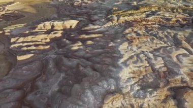 Utah 'taki Bentonite Hills' in engebeli ve renkli arazisini hava perspektifinden gösteren kaliteli bir video, karmaşık desenleri ve katmanları vurguluyor.