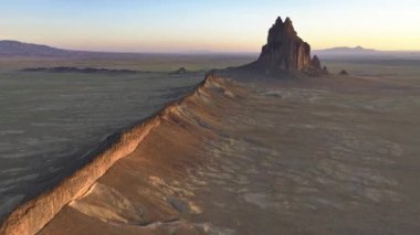 Günbatımının altın ışığı altında Shiprock anıtının çarpıcı hava aracı görüntüsü New Mexico 'nun engin ve engebeli manzarasını gözler önüne seriyor..