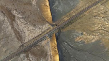 Bir İHA, Shiprock, New Mexico 'daki kuru ve dokulu bir arazinin içinden geçen bir yolu görüntüler. Video, toprağın barışçıl ama katıksız doğasını gerçek zamanlı olarak vurguluyor. Gri yoldaki dünyevi tonlarla çelişiyor..