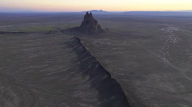 Hava aracı görüntüleri New Mexico 'daki görkemli Shiprock' u çekiyor, günbatımının renkleriyle yıkanmış, bu ikonik taşın etrafındaki geniş, dokulu manzarayı gösteriyor..