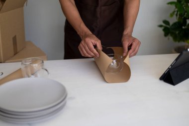 Tabaklar ve tabletlerle dolu bir masada cam bardağı kahverengi kağıda sarıp paketlemeye hazırlanan tanınmamış bir insan..