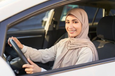 Güzel, genç Müslüman peçeli kadın araba sürerken mutlu bir şekilde gülümsüyor.