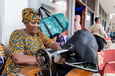 Geleneksel kıyafetleri olan Afrikalı bir kadın şehrin dışında geleneksel bir makineyle dikiş dikiyor.