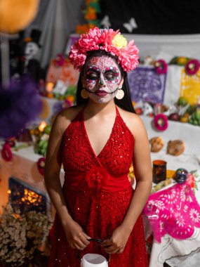 A young Hispanic woman dressed as a catrina is posing in front of an altar during day of the dead celebration. Concept of traditional Dia de Muertos in Mexico clipart