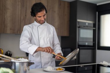 Profesyonel bir aşçı, tavadan tabağa yemek servisi yapan beyaz bir önlük giyer ve yemek hazırlar..