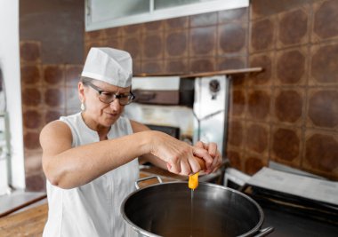 Beyaz üniformalı ve aşçı şapkalı bir kadın fırıncının portresi ticari bir mutfakta yumurta karıştırıyor.