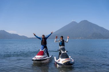 Genç İspanyol erkekler, Guatemala 'daki Atitlan Gölü' nün arka planına karşı dinamik ve enerjik bir sahne yaratarak jet skiler üzerinde poz veriyorlar.