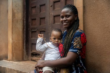 Afrikalı bir anne küçük oğlunu sevgiyle kucağına alır. Hem gülümser, hem de huzurlu bir anın tadını çıkarır. Kameraya bakar..