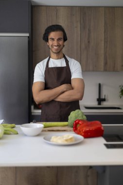 Çağdaş bir mutfakta kolları kavuşturulmuş, sebzeler tezgahta duran bir şef..