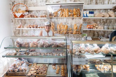 Beyaz üniformalı ve aşçı şapkalı, fırında kameraya gülümseyen mutlu ve gururlu bir beyaz kadın fırıncının portresi.