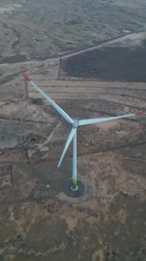 Günbatımında engin ve kuru bir arazide duran yalnız bir rüzgar türbininin hava görüntüsü yenilenebilir enerji sektöründeki güvenlik denetimlerini vurguluyor.