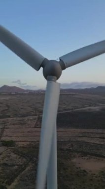 Alacakaranlıkta engin bir çöl manzarasına yerleştirilmiş bir rüzgar türbininin yakından görüntüsü, açık bir gökyüzüne karşı muazzam büyüklükteki türbinlere odaklanıyor.