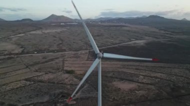 Çorak ve seyrek bir arazinin ortasında duran ve yenilenebilir enerji tesislerinin izolasyonunu ve ölçeğini vurgulayan tek bir rüzgar türbini gösteren bir hava görüntüsü.