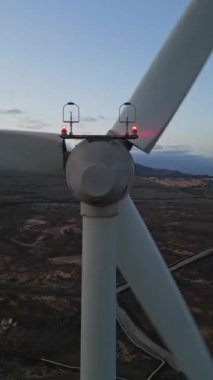 Günbatımında çekilen ve yenilenebilir enerji teknolojisinin altını çizen bir rüzgar türbininin videosu. Türbin, devasa bıçaklarını aydınlatan loş bir gökyüzüne karşı duruyor.