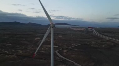 Alacakaranlıkta hava perspektifinden bir rüzgar türbini yakalayan, engin ve uzak bir arazide heybetli boyutunu gösteren bir düşük ışık videosu.