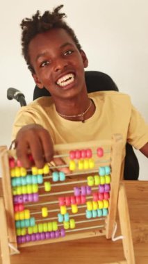 Serebral felçli genç bir birey, ahşap bir masada matematik kavramları öğrenmekle meşgul renkli bir abaküs üzerindeki boncukları saymaya odaklanıyor.