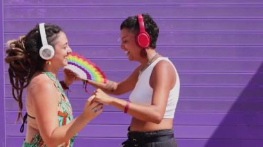 Lezbiyen bir çift güneşli bir günün tadını çıkarır. Renkli giysiler içinde dans ederler, aşkı ve neşeyi kutlarlar. Gururun ve LGBTQIA + topluluğunun mükemmel bir temsili.