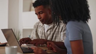 İnternetten alışveriş yapan genç siyah bir çift, dizüstü bilgisayar ve kredi kartı kullanıyor kahve fincanı olan bir masada oturuyorlar, ekran ve kart detaylarına odaklanmış durumdalar.