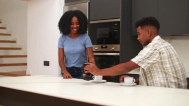 Mutlu siyah bir çift, modern bir mutfakta kahveyi hazırlarken ve tadını çıkarırken keyifli bir anı paylaşıyor. Parlak, gösterişli ortam rahatlatıcı ve neşeli atmosferi arttırır..