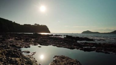 Güneş, Kosta Rika 'nın Papagayo Körfezi' nde batıyor. Kayalık kıyılarına sıcak bir parıltı saçıyor. Arka planda bir kayığın geçişini görebilirsiniz.