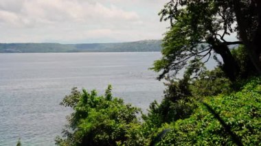 Golfo de Papagayo, Kosta Rika 'nın dingin güzelliğini keşfedin. Uçsuz bucaksız okyanus, yoğun bir yeşillikle çevrelenmiş, kısmen bulutlu bir gökyüzü altında, huzur ve doğanın cazibesini sunuyor.