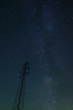 Sayısız yıldız ve Samanyolu 'nun belirsiz ipuçlarıyla dolu huzurlu bir gece gökyüzü. Önplanda uzun bir iletim kulesinin silüeti var.
