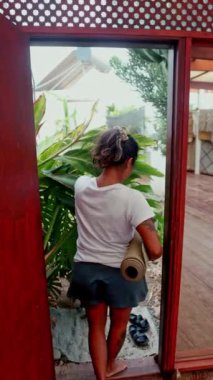 Bir insan elinde yoga minderiyle dışarıya adım atar, sabah rutinine sakin bir şekilde dışarıda başlar. Sahne rahatlatıcı ve sağlıklı bir yaşam sunar.