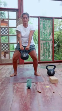 Bir insan, doğal ışık ve bitkilerle çevrili huzurlu bir yoga stüdyosunda kettlebell egzersizi yapar.