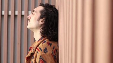 Bir adam dokulu bir duvara yaslanır, yansıma ve sükuneti somutlaştırarak sakin bir yaşam tarzını yakalar, rahatlama ve farkındalığı vurgular.