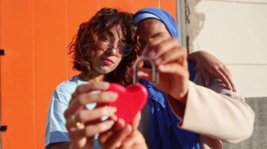 Müslüman bir partner de dahil olmak üzere çok kültürlü bir lezbiyen çift, kalp şeklinde bir sembol taşıyor. Bu video LGBTQIA + topluluğu içindeki sevgi ve çeşitliliği kutluyor.