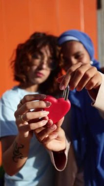 Müslüman bir partner de dahil olmak üzere çok kültürlü bir lezbiyen çift, kalp şeklinde bir sembol taşıyor. Bu video LGBTQIA + topluluğu içindeki sevgi ve çeşitliliği kutluyor.
