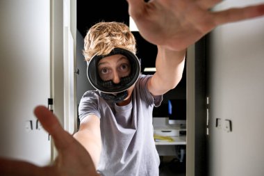 Neşeli bir ifadeye sahip genç bir çocuk, bir soyunma odasının içinde, sanki oyunla etkileşim halindeymiş gibi, bir VR kulaklık takarken görülüyor..