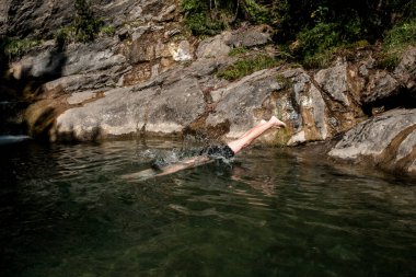 Canfranc, Huesca, İspanya 'da engebeli kayalarla çevrili doğal bir dağ havuzunun dingin ve berrak sularında yüzen bir insanın huzurlu bir görüntüsü.