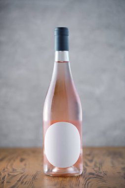 Ahşap bir yüzeyde boş etiketli zarif bir gül şarabı şişesinin yakın çekimi. Marka modellemeleri için ideal..