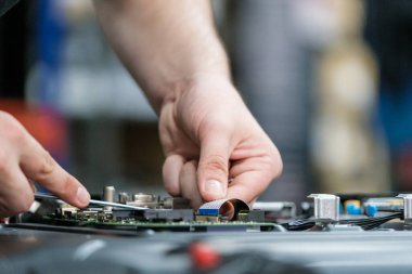 Bir teknisyenin ellerinin bir TV devre kartında ustalıkla çalışmasının yakın plan görüntüsü süreçte kullanılan hassasiyet, elektronik bileşenler ve tamir araçları üzerinde duruluyor.