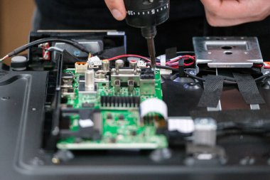 Bir televizyon devre kartının tamiri için matkap kullanan ellerin yakın plan çekimi, karmaşık kablolama ve elektronik bileşenler teknoloji ve tamir temaları için idealdir