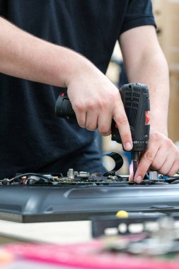 Televizyonu tamir etmek için matkap kullanan, elektronik bileşenlere odaklanan ellerin yakın çekimi teknik bakım çalışmaları için gereken hassasiyeti ve dikkati çeker.