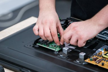 Bir teknisyen, karmaşık detaylar ve bağlantılar üzerine odaklanarak, bir televizyon devre kartını özenle onarır. Görüntü elektronik tamir becerileri ve teknoloji bakımını vurgular