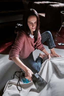 Bir kadın rahat ve rahat bir ortamda rahat ve rahat bir ortam yaratmak için rahat, sıcak ve aydınlık bir odada bir masa örtüsünü ustaca ütüler.