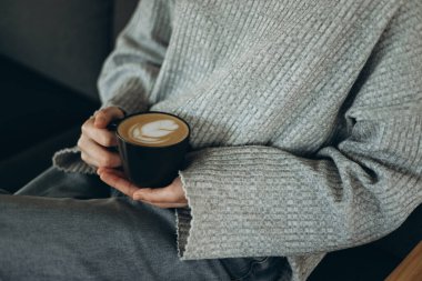 Rahat bir sahne, rahat giyinen birinin elinde karışık latte sanatıyla bir fincan kahve tutarken rahatlatıcı bir ortam yayar, kahve aşıkları için mükemmeldir.
