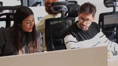 Bir erkek ve bir kadın iş arkadaşı ofis çalışma alanlarında iş birliği yaparak, yoğun bir ofis ortamında takım çalışması ve konsantrasyon sergilediler..