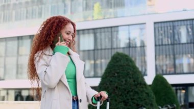 Karışık ırklı, kızıl saçlı, bavulunu çekerken telefonla konuşan, şehir içinde gezinen bir kadın. Sıradan, şık bir kıyafet giymişti..