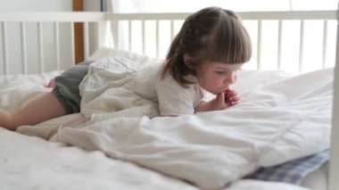 Küçük bir çocuk huzurlu bir anda beyaz bir yatak örtüsüne uzanmış küçük ellerine odaklanmış olarak yakalanır. Pencereden gelen doğal ışık onun konsantre ifadesini ve sakinliğini vurguluyor..