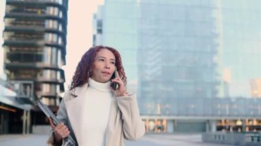 Şehir ortamında karışık bir yarış kadını elinde dizüstü bilgisayarla bir telefon görüşmesi yapıyor. Modern şehir hayatı ve profesyonel bağlılığı somutlaştırıyor..