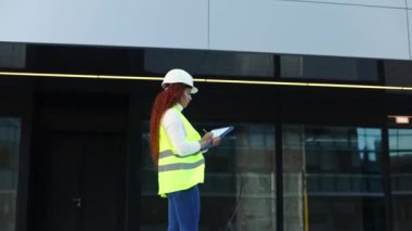 Sert şapkalı ve neon yelekli melez bir Latin kadın şehir caddesi boyunca yürüyor. Bir pano tutuyor, modern mimari ile çevrili, kentsel profesyonel hayatı gösteriyor..