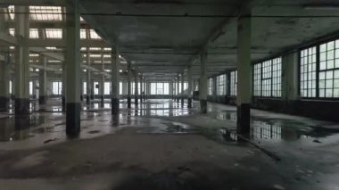 Yerdeki sanayi yapısını yansıtan loş ışıklandırma, geniş pencereler ve su birikintileriyle terk edilmiş bir fabrikanın içi. Karamsar ve atmosferik bir titreşim uyandırır..