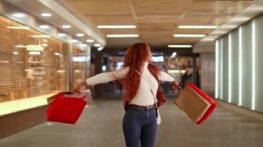 Kıvırcık saçlı, alışveriş torbaları taşıyan mutlu ırk kadını. Şehir geçidinde yürüyor, şehirde bir gün boyunca canlı bir şehir atmosferinin tadını çıkarıyor..