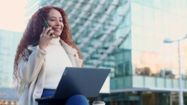 Akıllı telefonu ve dizüstü bilgisayarı ile şehir ortamında melez bir kadın. Meşgul ve odaklanmış görünüyor, modern şehir mimarisinin bir zeminine göre ayarlanmış..